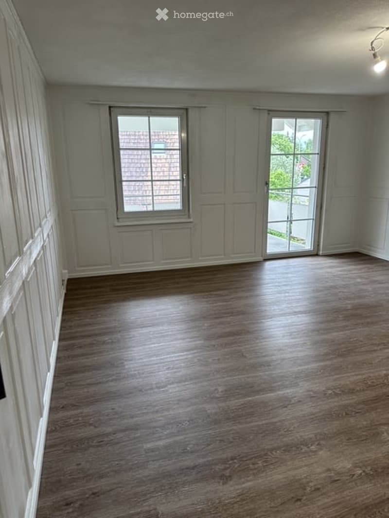 Empty room with wooden flooring, large windows, and white walls. No furniture or equipment present.
