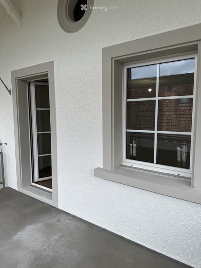 White exterior wall with a large window and a glass door leading to a balcony or terrace area.