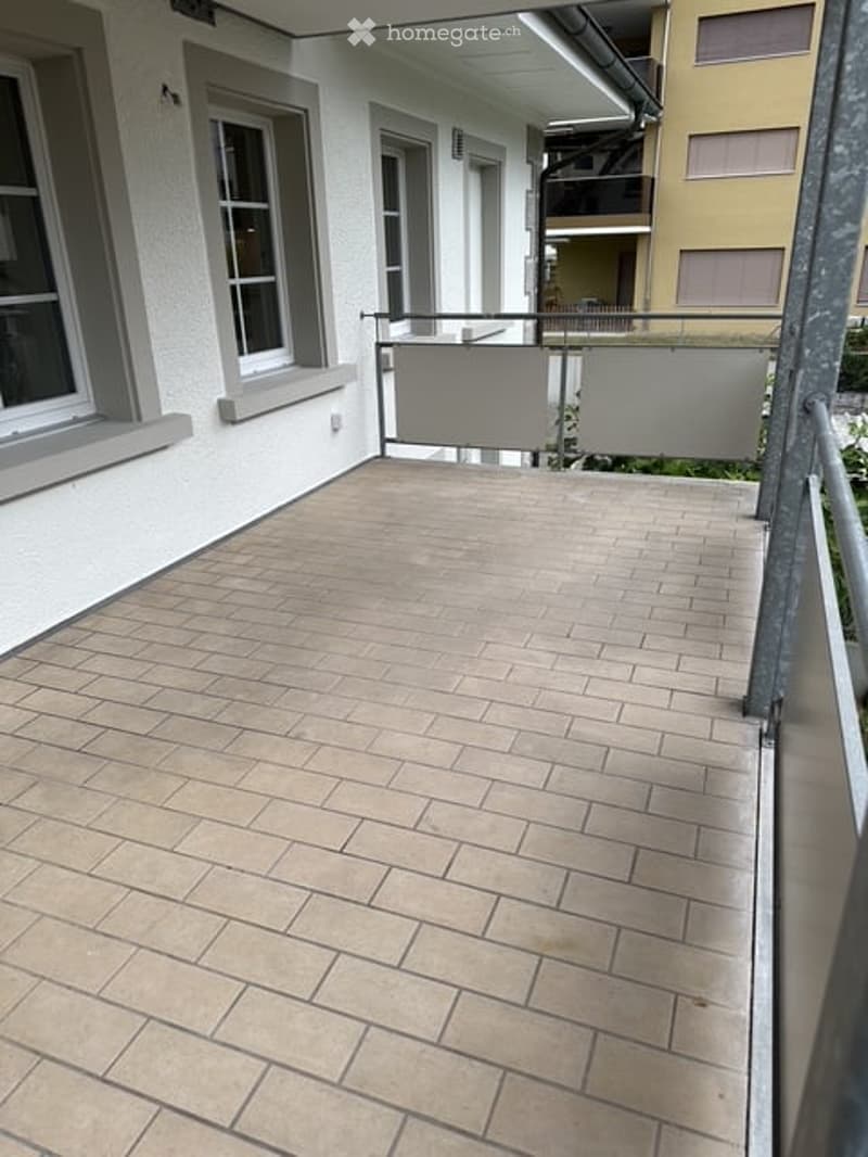 Balcony with tiled floor, metal railing, and large windows on the adjacent building.