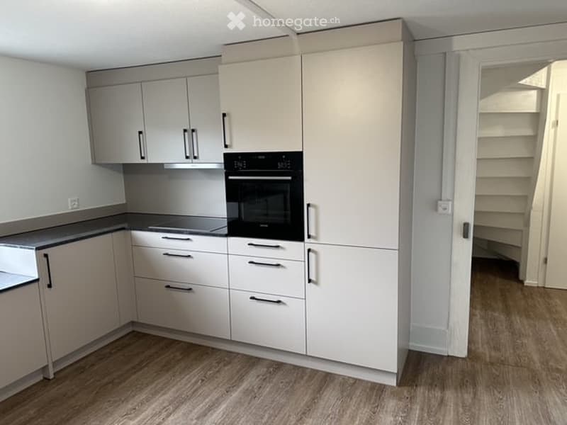 Modern kitchen with white cabinets, a built-in oven, and a sleek countertop. The space features light wood flooring and ample storage.
