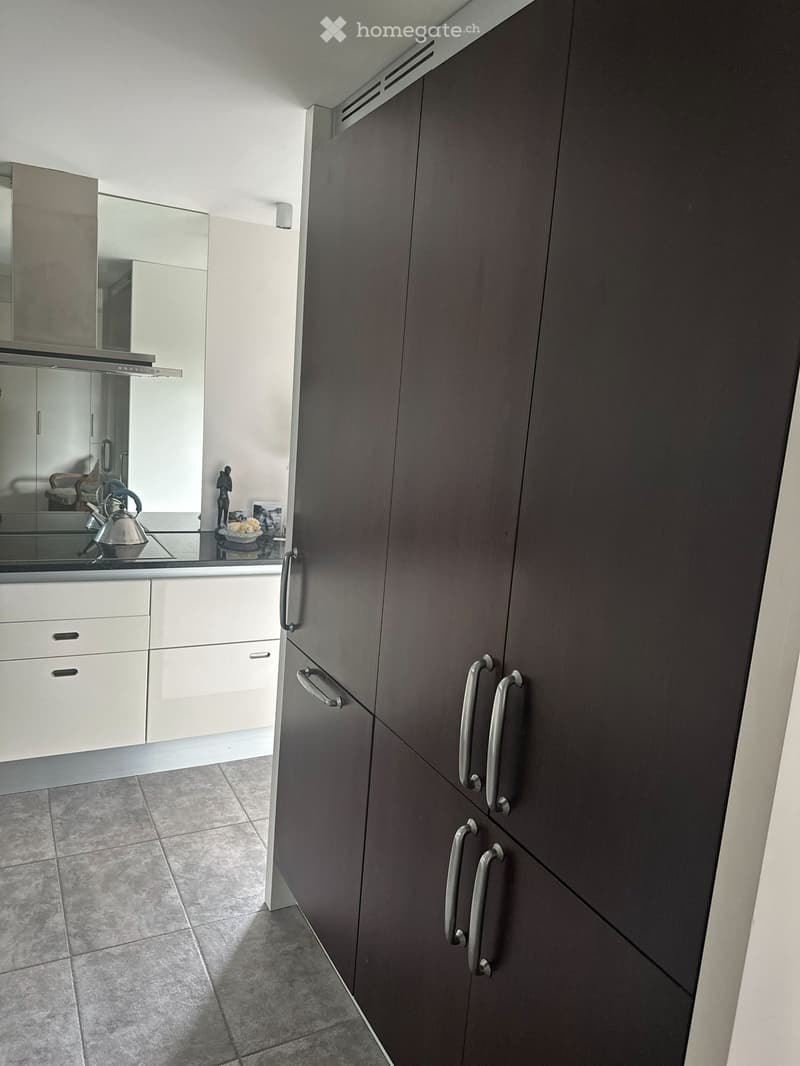 Modern kitchen with dark grey cabinets, white lower cabinets, tiled floor, and a reflective countertop with a teapot, bowl, and small statue.