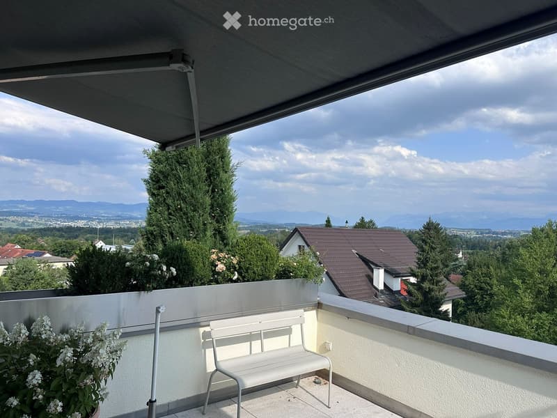 Balcony with a white bench, potted plants, and a retractable awning, overlooking a scenic landscape with trees and distant mountains.