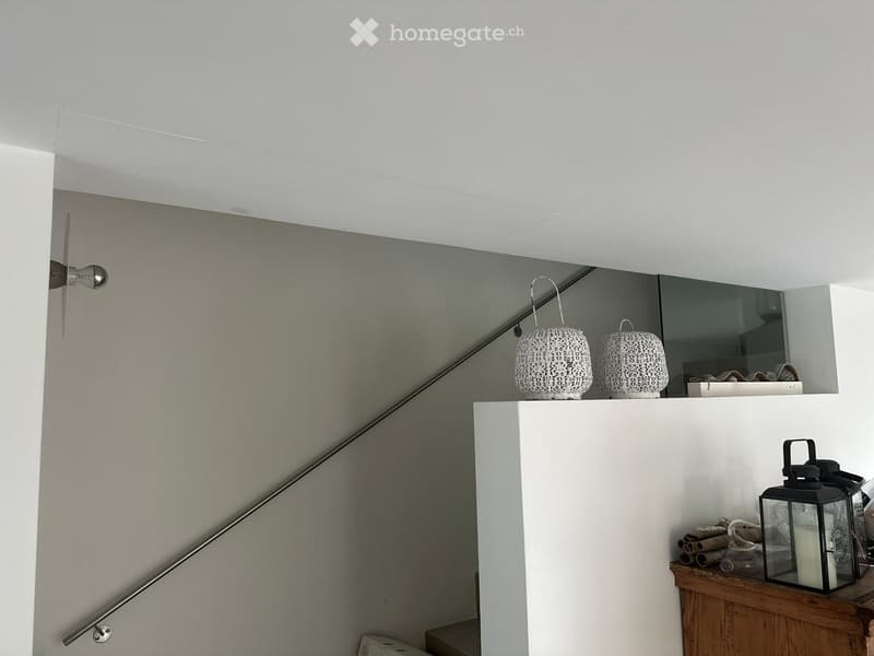 Modern hallway with white walls, a sleek metal handrail, and decorative items including woven baskets and a lantern on a wooden shelf.