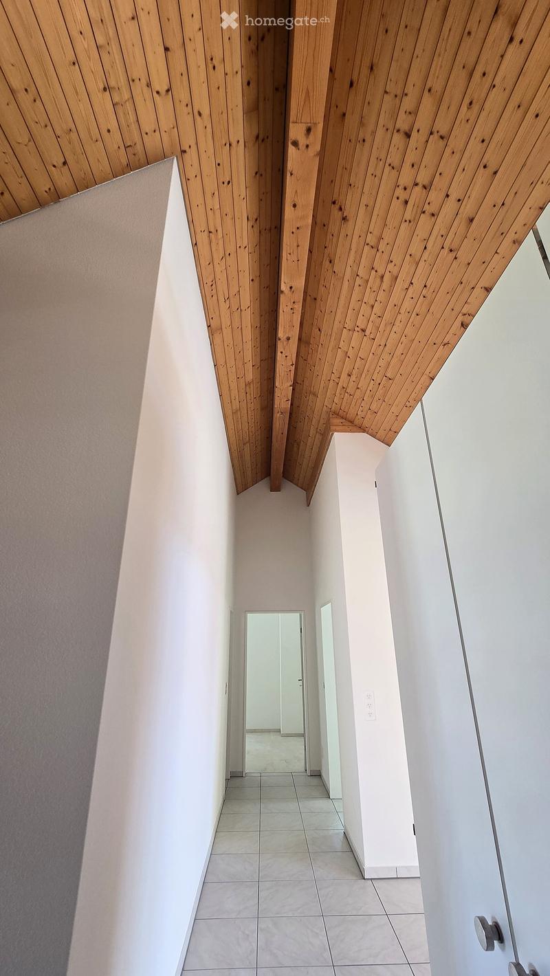 Modern hallway with white walls, tiled floor, and wooden slatted ceiling. Features a mirror and a light switch on the wall.