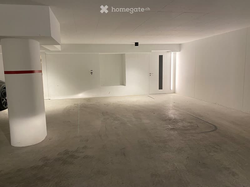 Empty underground parking space with concrete floor, white walls, and a single support column. No vehicles or furniture present.