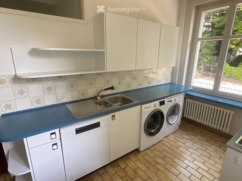 Modern kitchen with white cabinets, blue countertop, stainless steel sink, and built-in washing machine and dishwasher.