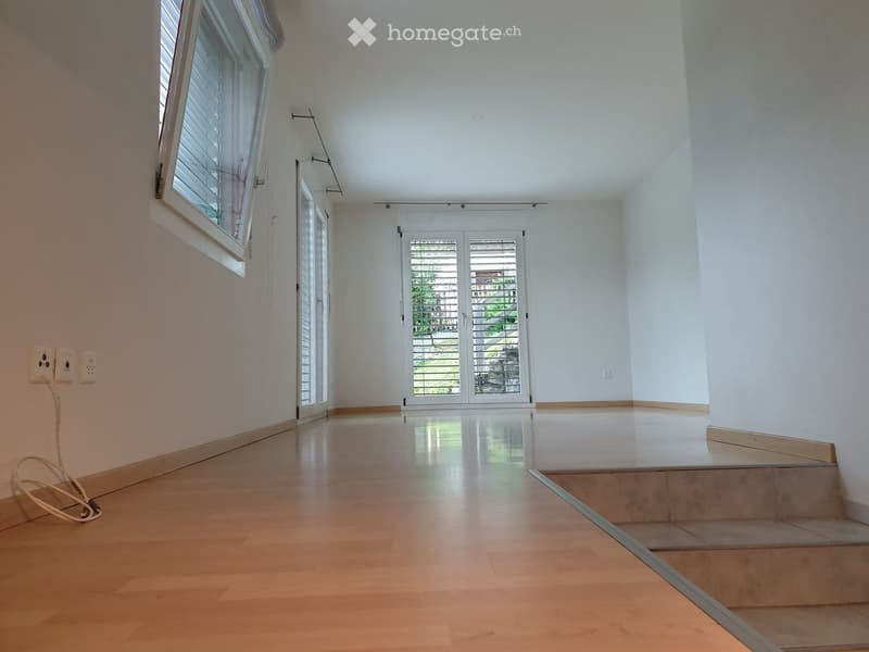 Empty hallway with wooden flooring, white walls, large windows, and a sliding glass door leading outside.