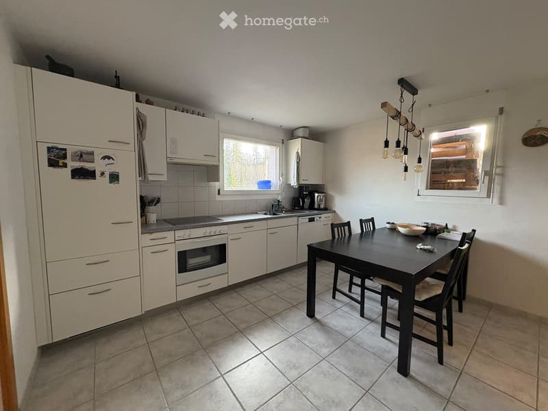 Bright kitchen with white cabinets, tiled floor, and a dining area featuring a black table and chairs. Appliances include a refrigerator, oven, dishwasher, and coffee maker.