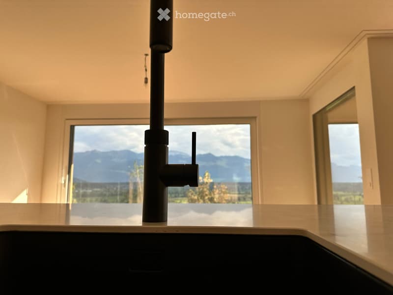 Modern kitchen with a sleek black faucet on a light-colored countertop, large windows offering a scenic mountain view.