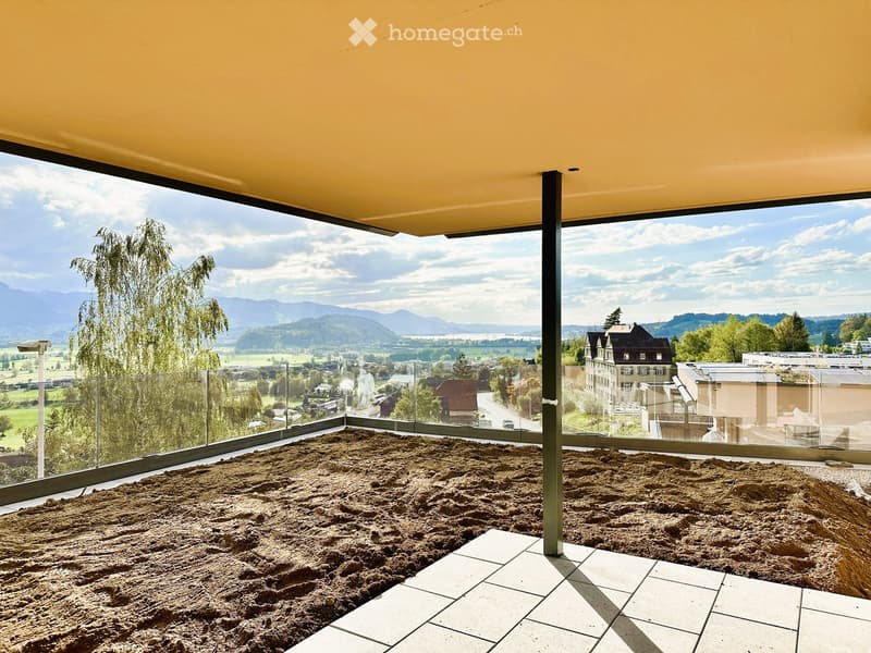 Empty balcony with a panoramic view of a valley and mountains, featuring a glass railing and tiled floor.