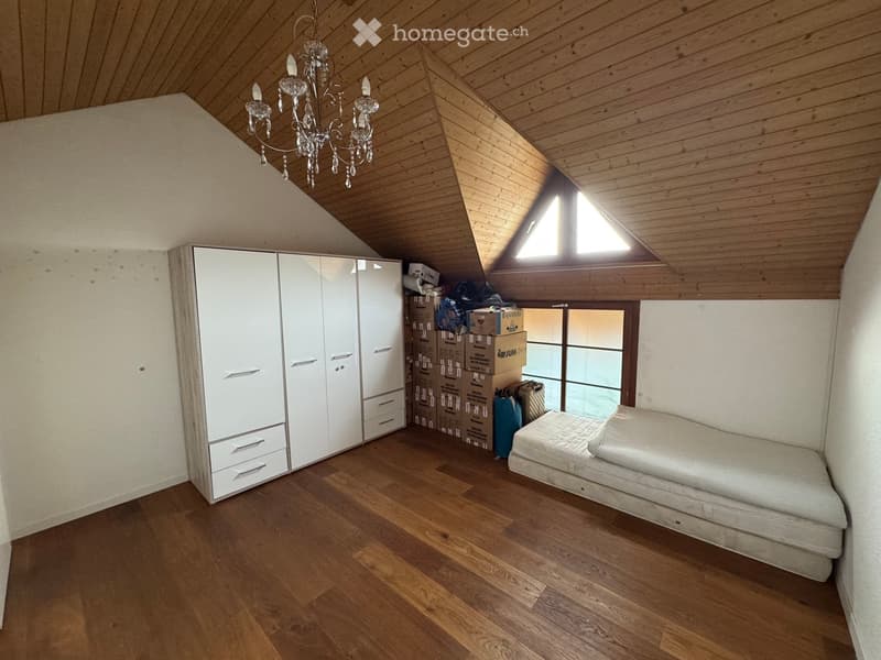 Spacious attic room with wooden floors, white built-in wardrobe, a bed, and a chandelier. The room features exposed wooden beams and a skylight window.