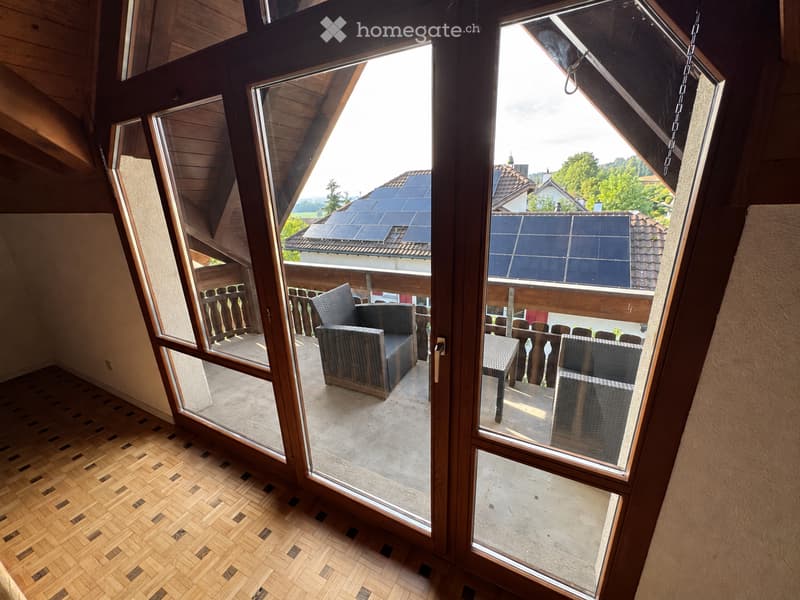 A room with wooden flooring and large glass doors leading to a balcony with outdoor furniture.