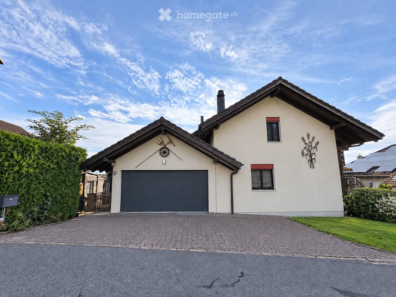 Two-story house with a gray garage door, white walls, and decorative corn stalk wall art. The house features a paved driveway and is surrounded by greenery.