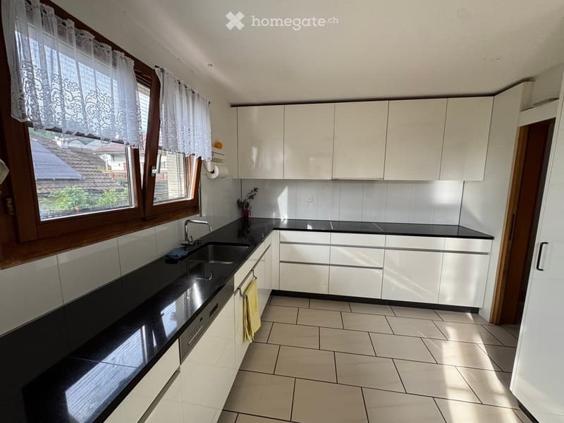 Modern kitchen with white cabinets, black countertops, and a large window with lace curtains. Features a sink, faucet, and a towel hanging from a cabinet.