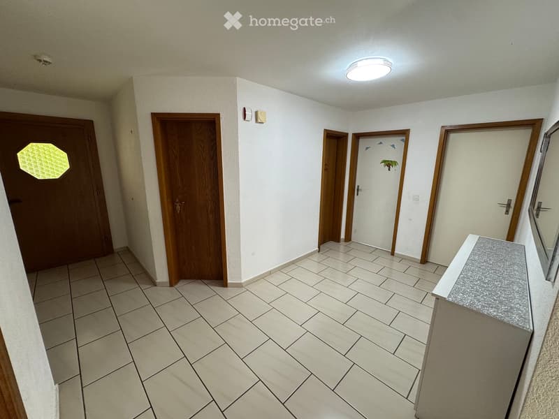Empty hallway with tiled floor, white walls, multiple wooden doors, and a round ceiling light fixture.