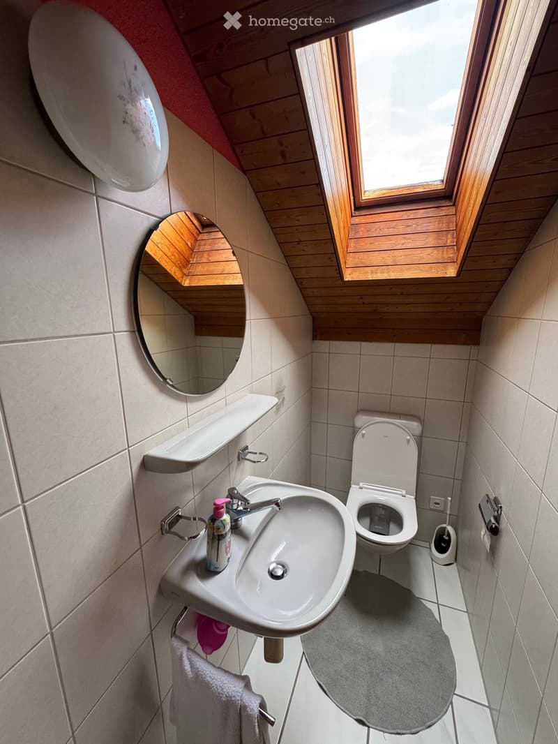 Compact bathroom with a sink, toilet, mirror, and towel. Features a window with wooden frame and a small shelf above the sink.