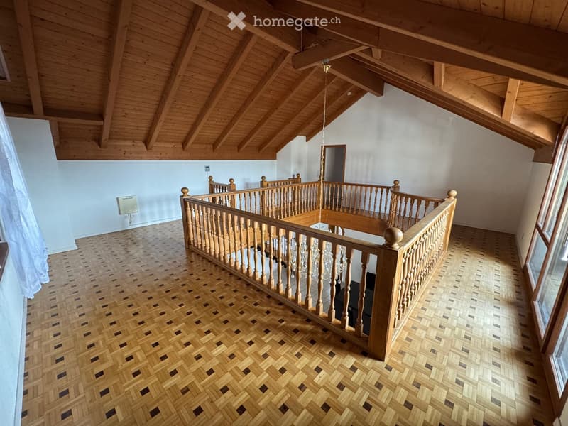 Spacious hallway with wooden floors, exposed wooden beams, and a wooden railing leading to an upper level.