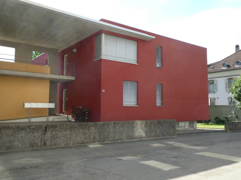3-story apartment building, red exterior walls, balconies, covered entrance, bicycles parked outside
