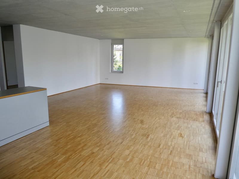 Large open space with hardwood flooring, white walls, and a window providing natural light. The room appears to be empty, ready for furnishing and use.