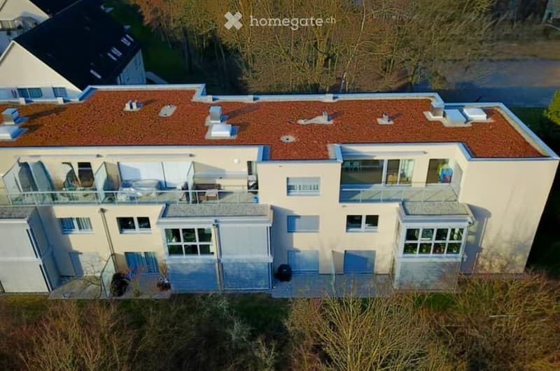 Modern two-story house with a red-tiled roof, multiple balconies, large windows, and a flat roof terrace area.