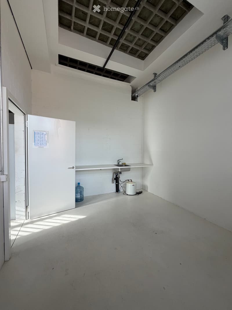 Empty room with white walls, concrete floor, small sink, water tank, and a water bottle on the floor.