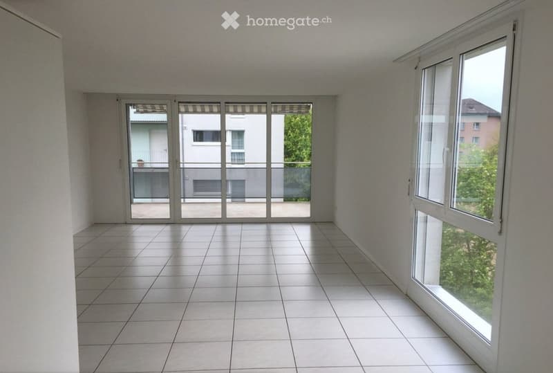 Empty room with tiled floor, large windows, and sliding glass doors leading to a balcony.