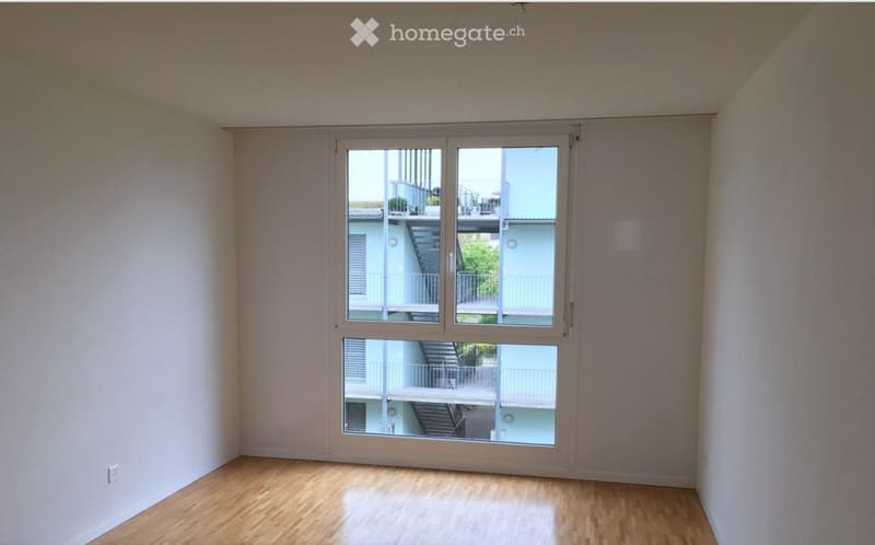 Empty room with wooden flooring and large windows showing a view of a staircase and outdoor area.