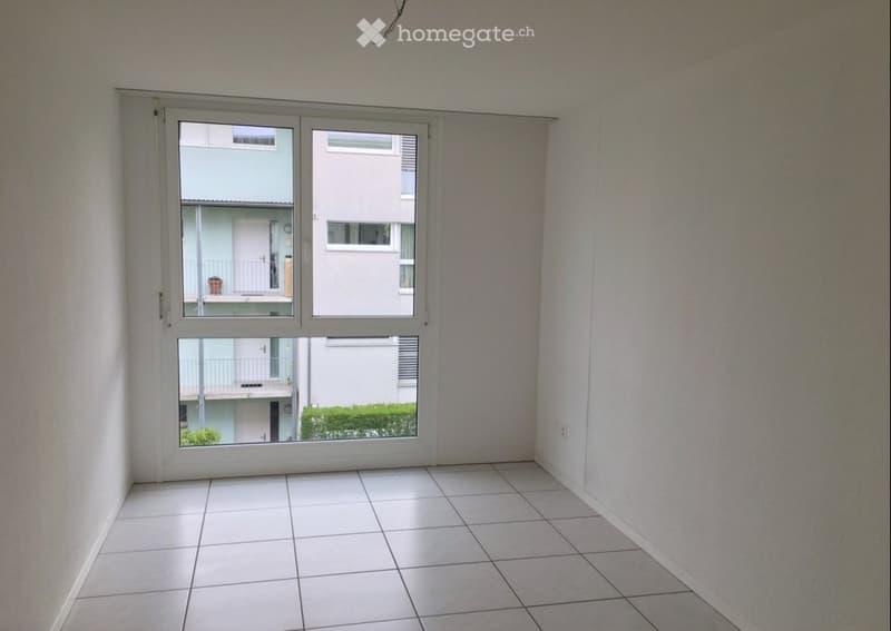 Empty room with white tiled floor and large window showing neighboring buildings and greenery.