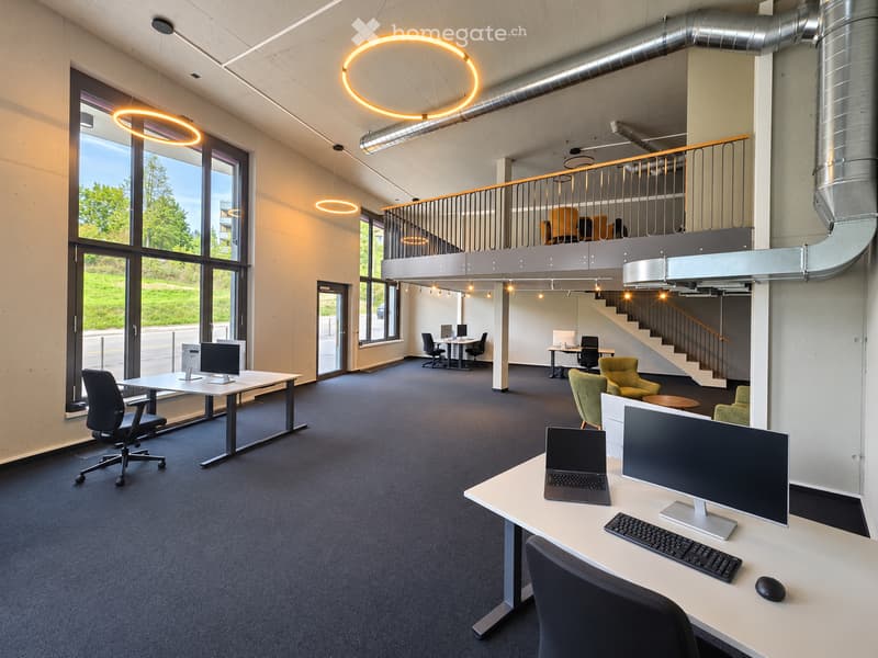 Modern office space with desks, chairs, computers, and a staircase leading to an upper level.