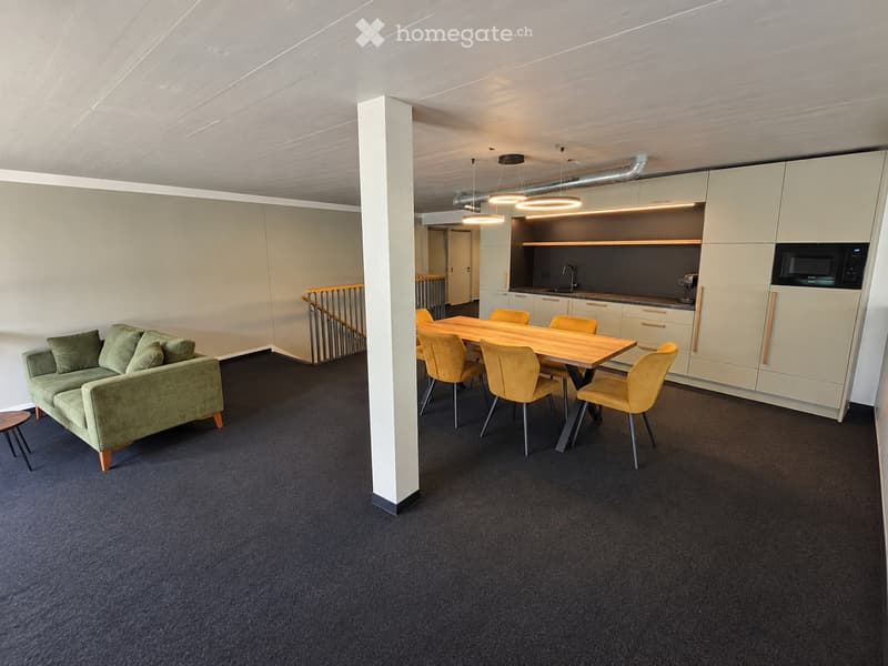 Modern, open-plan room with a green sofa, wooden dining table, yellow chairs, and a compact kitchen area featuring white cabinets, a microwave, and a sink.