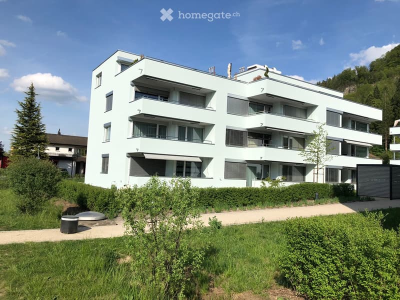 white apartment building, 4 stories, balconies on each floor, concrete walkway, green grass