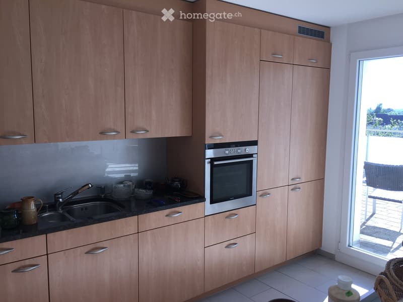 Modern kitchen with light wooden cabinets, stainless steel oven, and black countertop. Includes sink, faucet, and various kitchen items.