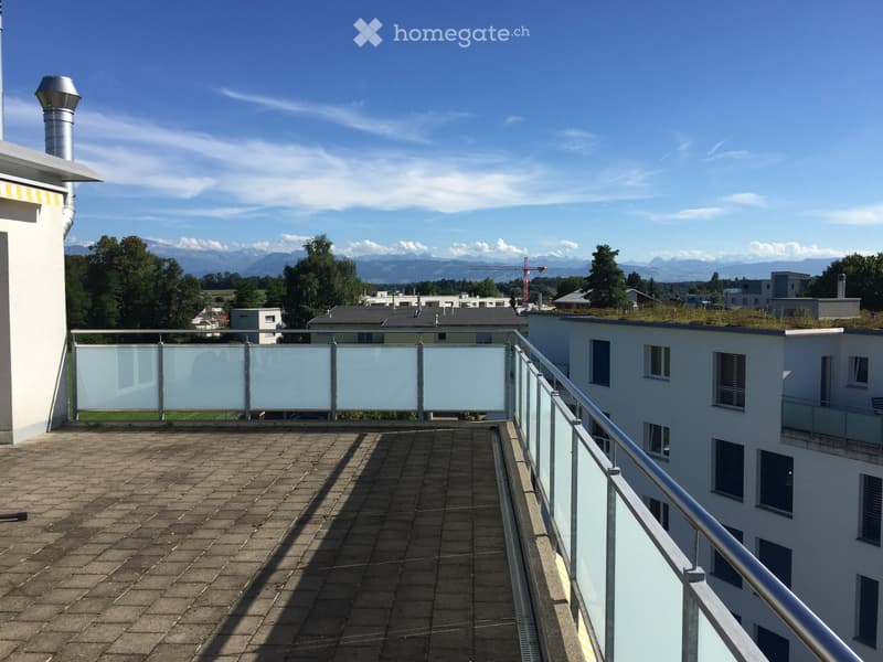 Roof terrace with tiled surface, glass railing, and distant mountain view.