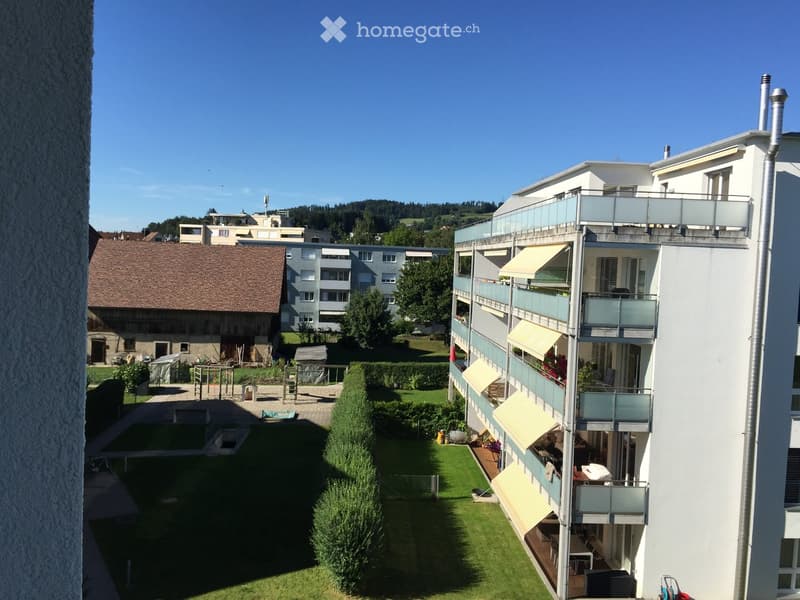 Multi-story residential building with balconies, awnings, and a well-maintained garden area with a swimming pool and playground.