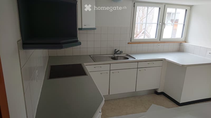 Modern kitchen with white cabinets, a stainless steel sink, and an electric stove. The space is clean and well-lit with natural light from the window.