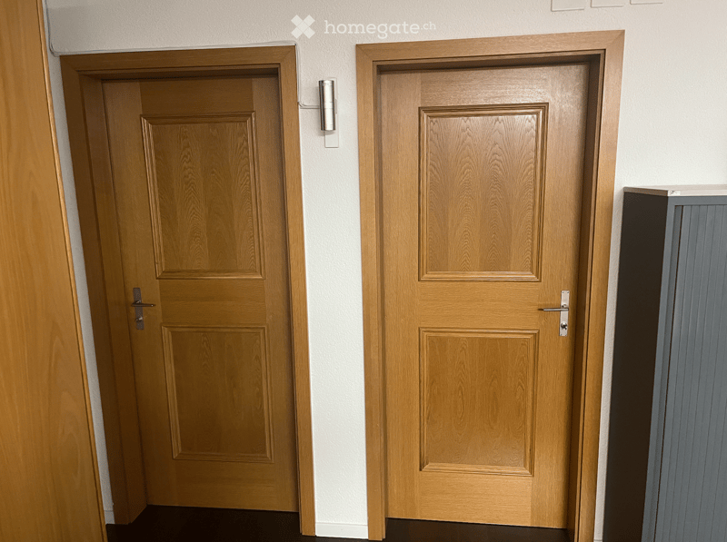 Two wooden doors in a white room, a wall-mounted light is visible between the doors.
