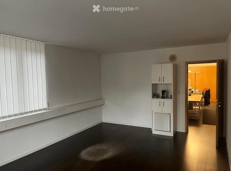 empty room, white walls, dark wooden floor, window with venetian blinds, small cabinet in corner, open door to another room