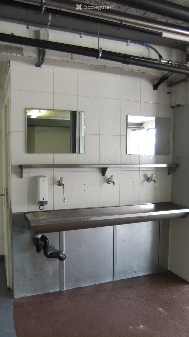 Industrial-style bathroom with stainless steel sink, multiple faucets, mirrors, and a soap dispenser.