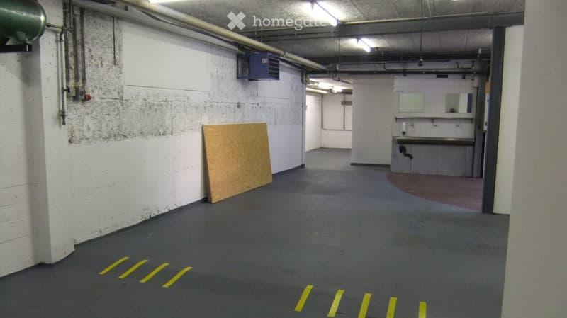 Empty hallway with white walls, grey carpeted floor, and yellow parking lines. A small utility area with a sink and mirror is visible at the end.