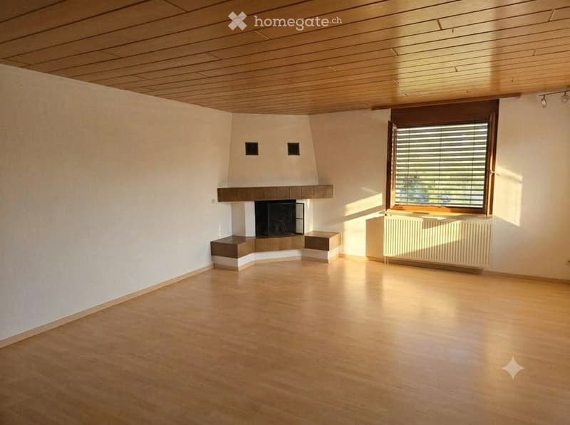 Empty room with wooden flooring, white walls, a fireplace, and a large window with blinds.