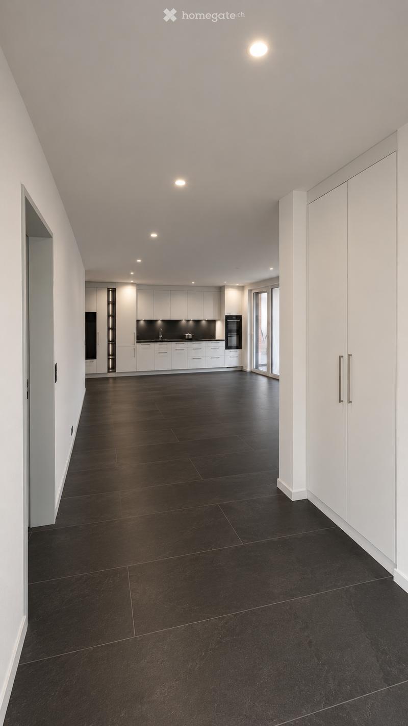 Empty kitchen with white cabinets, black countertops, and dark tiled flooring. No furniture or appliances are present.