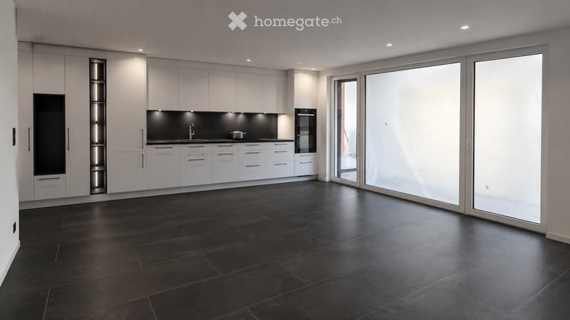 Modern kitchen with white cabinets, dark countertops, and large windows. Features include a sink, oven, and sleek design.