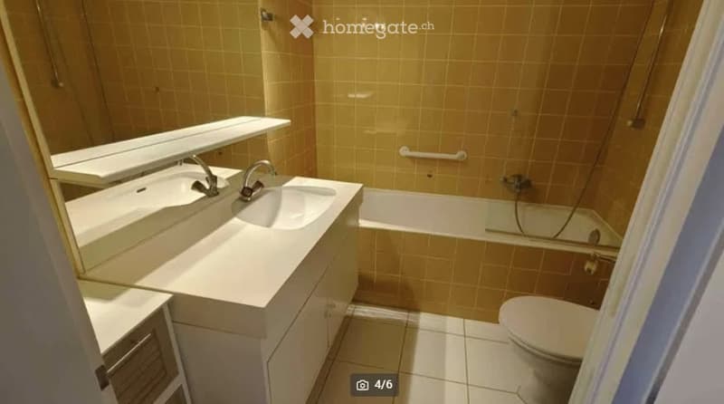 Modern bathroom with double sink, large mirror, bathtub, and toilet. Light-colored tiles and clean, contemporary design.