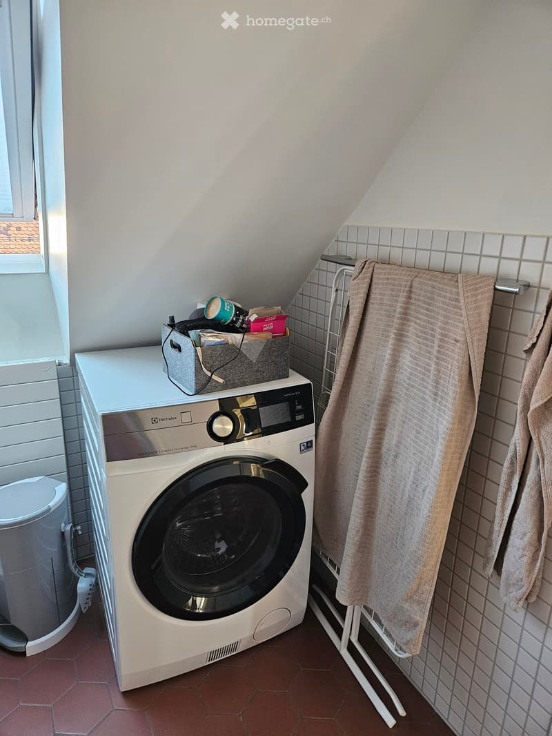 A small bathroom with a washing machine, a towel rack with towels, and a laundry basket on top of the washing machine.