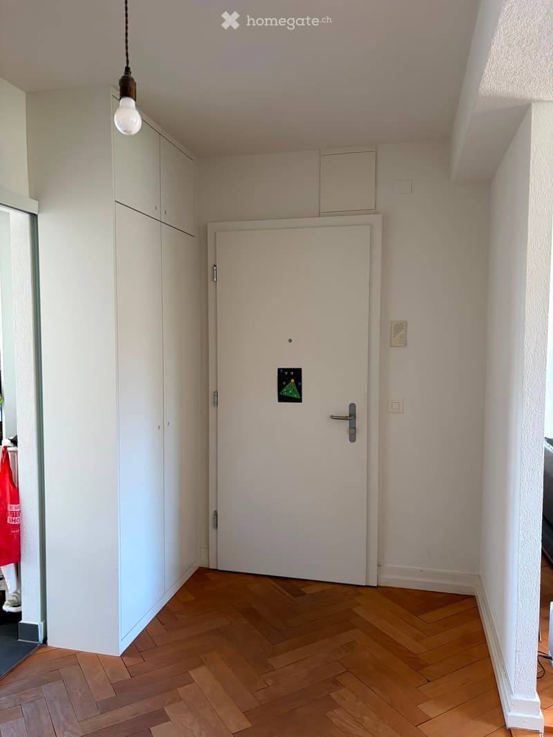 Empty hallway with wooden flooring, white walls, built-in white cabinets, and a closed white door.