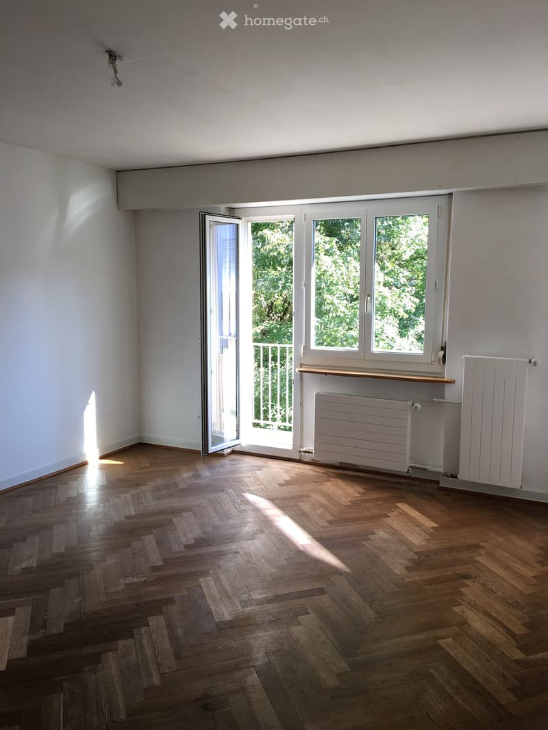 Empty room with wooden flooring, white walls, large windows, and a sliding glass door leading to a balcony.