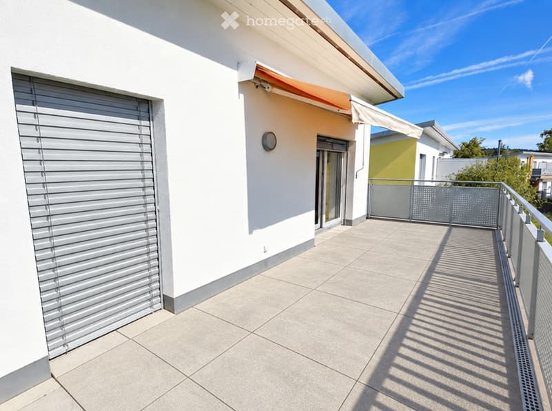 Balcony with tiled floor, metal railing, and awning attached to a white building.
