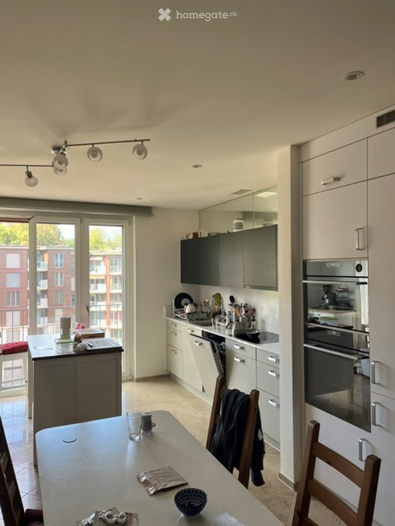 Modern kitchen with white cabinets, stainless steel appliances, and a large window offering a view of the building outside.
