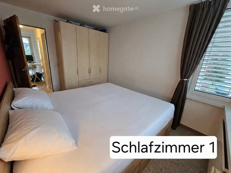 Well-lit bedroom with a double bed, pillows, a large wardrobe, and a window with blinds.