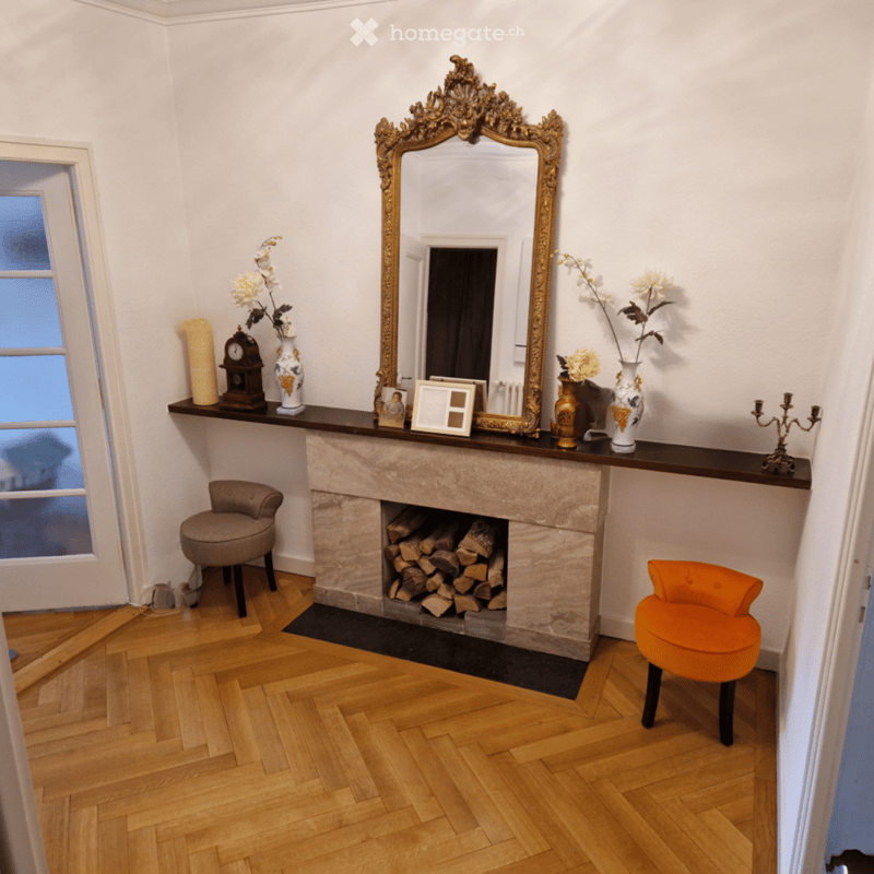 Elegant living room with a stone fireplace, two colorful stools, ornate mirror, decorative vases, and a candle holder on the mantel.